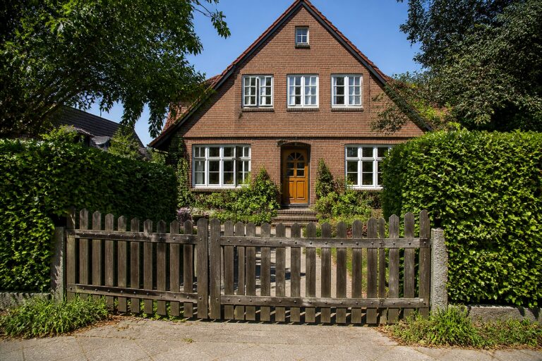 Einfamilienhaus mit Holztor und Hecke im Nachmittagslicht